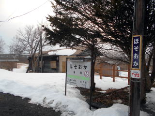 細岡の駅名標。駅前にある唯一の建物は集会所だが、窓ガラスの所は板で塞がれてしまい、使われなくなった印象を受ける。