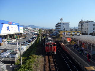 大歳を発車した山口線のディーゼルカー。遠方にはレノファ山口のホームスタジアムである、維新みらいふスタジアムが見える。