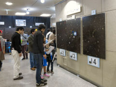 壁に貼られた天体写真と手元の問題用紙の銀河写真を見比べる人たち